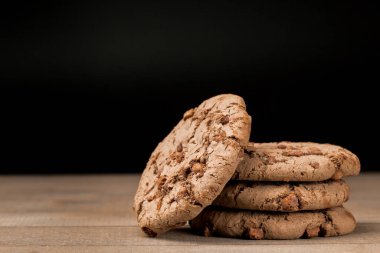 Kahverengi çikolatalı kurabiye büyük poan. Siyah bir arka planda. Kahverengi çikolata parçalı çikolatalı kurabiyeler ahşap bir masaya konur..