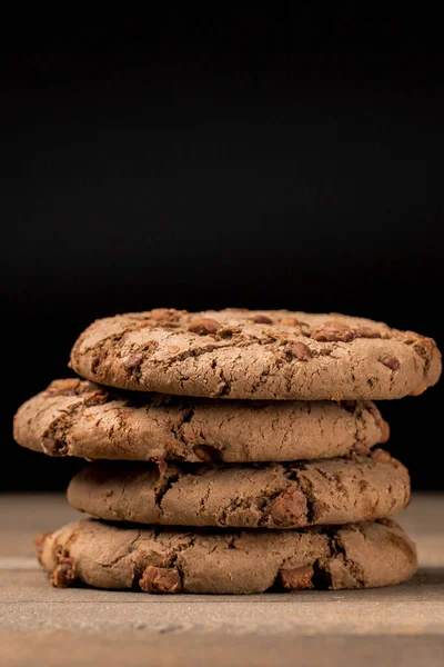 Kahverengi çikolatalı kurabiye büyük poan. Siyah bir arka planda. Kahverengi çikolata parçalı çikolatalı kurabiyeler ahşap bir masaya konur..