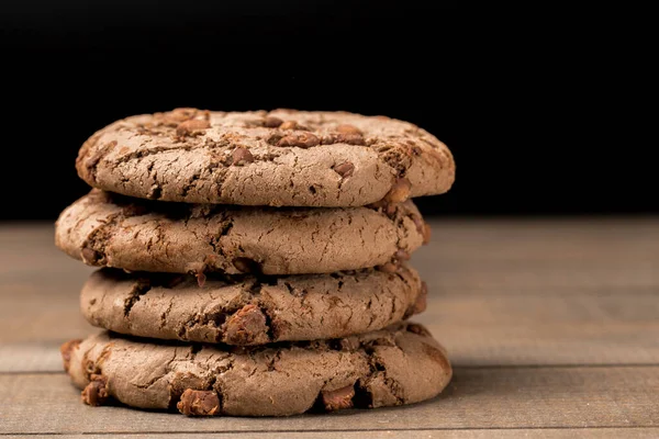 Kahverengi çikolatalı kurabiye büyük poan. Siyah bir arka planda. Kahverengi çikolata parçalı çikolatalı kurabiyeler ahşap bir masaya konur..