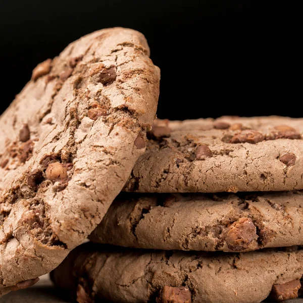 Kahverengi çikolatalı kurabiye büyük poan. Siyah bir arka planda. Kahverengi çikolata parçalı çikolatalı kurabiyeler ahşap bir masaya konur..