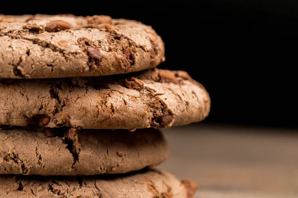 Kahverengi çikolatalı kurabiye büyük poan. Siyah bir arka planda. Kahverengi çikolata parçalı çikolatalı kurabiyeler ahşap bir masaya konur..