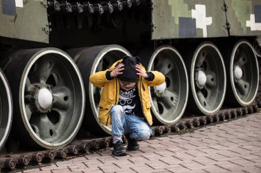 Ukrayna 'da savaş, patlamalardan saklanan çocuk. Tank ve obüs Ukrayna' da sokakta duruyor. Kiev parkında bir silah ve yeşil bir tank var..