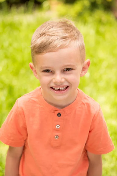 5歳の少年が顔を作っている 晴れた日に道に立っていると 五歳の金髪の少年が顔を出す — ストック写真