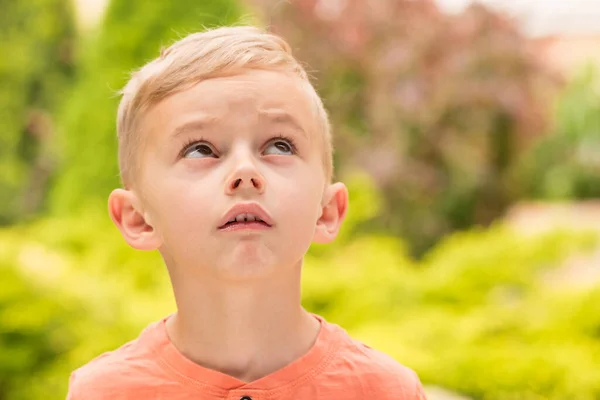Beş yaşında bir çocuk surat yapıyor. Beş yaşında sarışın bir çocuk güneşli bir havada sokakta dikilirken surat asıyor..