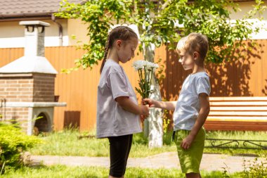 Altı yaşındaki bir oğlan bir kıza bir buket çiçek verir. Güneşli bir günde, bahçede oğlan kıza bir buket papatya verir..