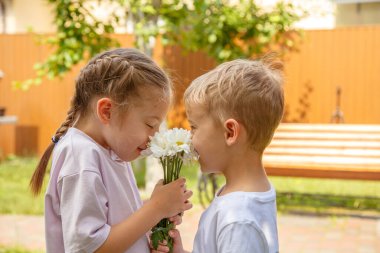 Altı yaşındaki bir oğlan bir kıza bir buket çiçek verir. Güneşli bir günde, bahçede oğlan kıza bir buket papatya verir..