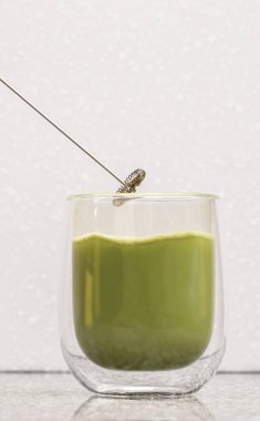 Green matcha latte tea in a glass. Green matcha latte is poured into a transparent glass with a double bottom