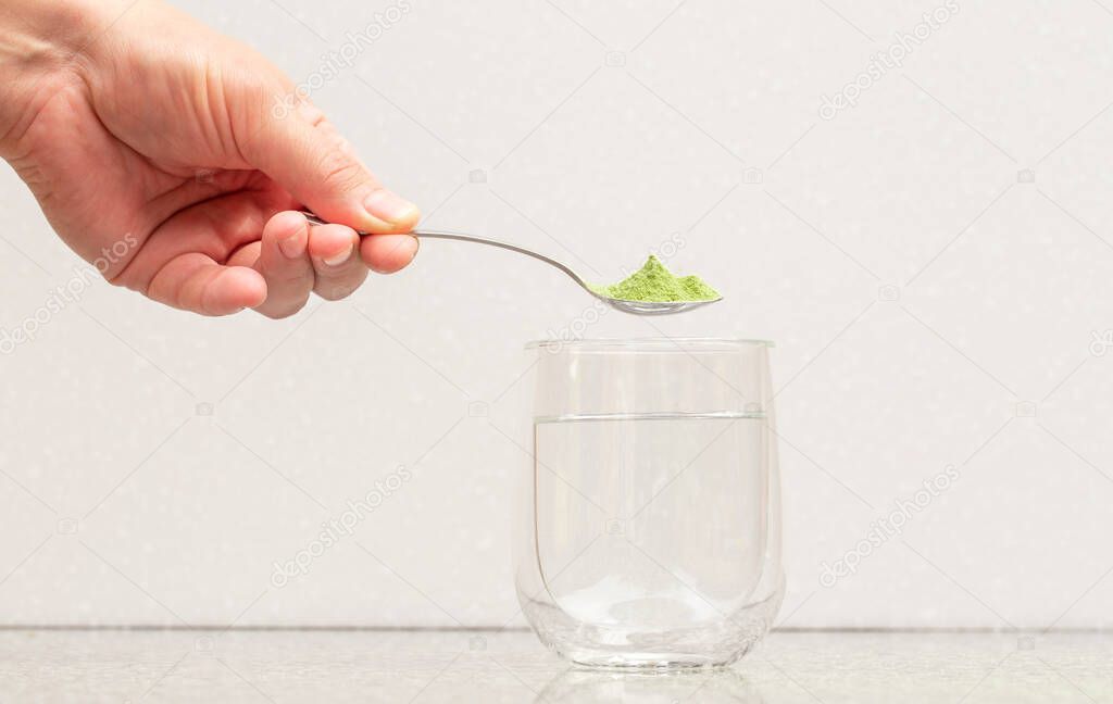 Green powder in a spoon (matcha tea) over a clear glass.