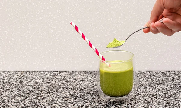 Matcha tea in a glass cup with a red straw stands on a steel and in the background a blurred background of the kitchen 