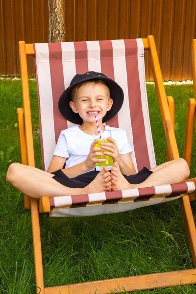 A boy and a girl are sitting on sun loungers in the garden on the grass. On a summer sunny day, a girl and a boy of six years old (of European appearance) are relaxing in the garden on sun loungers