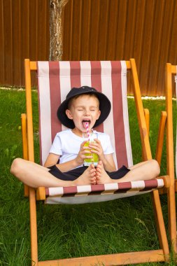 On a sunny summer day, a girl and a boy of six years old (of European appearance) are relaxing in the garden on deck chairs and drinking a green drink.