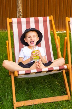 On a sunny summer day, a girl and a boy of six years old (of European appearance) are relaxing in the garden on deck chairs and drinking a green drink.