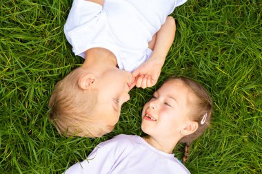 Çocuklar çimlere uzanıp gökyüzüne bakarlar. Avrupa görünümlü altı yaşında bir erkek ve kız çocuğu yeşil gazın üzerinde farklı pozlarda yatıyor..