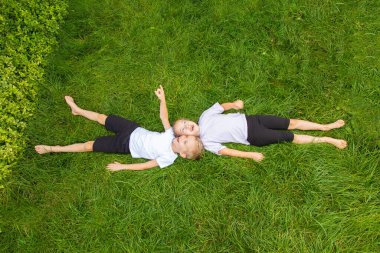 Çocuklar çimlere uzanıp gökyüzüne bakarlar. Avrupa görünümlü altı yaşında bir erkek ve kız çocuğu yeşil gazın üzerinde farklı pozlarda yatıyor..