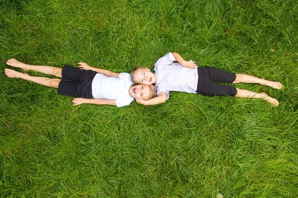 Çocuklar çimlere uzanıp gökyüzüne bakarlar. Avrupa görünümlü altı yaşında bir erkek ve kız çocuğu yeşil gazın üzerinde farklı pozlarda yatıyor..
