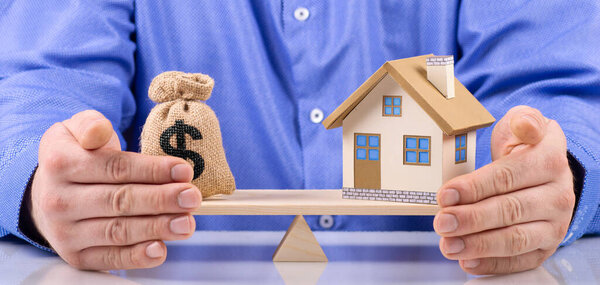 агент держать мешок с табличкой доллара и дома положить на весы с балансом сбережений или кредит на покупку нового дома или план бизнес-инвестиционной концепции.