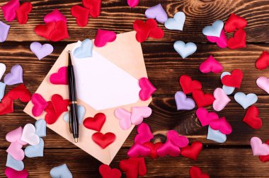 Aşk mektubu. Ahşap zemin üzerinde bir sürü kırmızı, pembe beyaz kalp ve siyah kalem olan eski bir zarf.