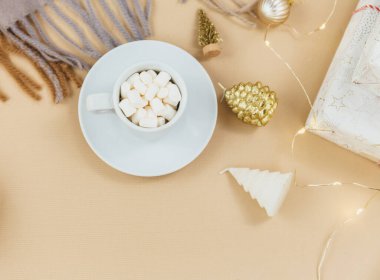 Bir fincan kahve, hediye kutusu ve örgü eşarp, bej arka planda ışık. Hygge tarzı, kış konsepti. Rahat ev masası. Yeni yıl ve Noel kutlaması modeli. Noel sakin hayat
