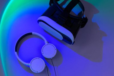 Mor arka planda yeşil ışıklı sanal gerçeklik gözlükleri ve kulaklıklar. Oyunlara hazır ol, siber sporcu. Üst görünüm