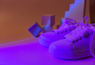Geometri podyumunda soyut parlak arka planda moda beyaz spor ayakkabıları. Sıradan ayakkabılarda neon ışıkları. Mor ve turuncu gradyan ışık. Minimalizm, 90 'lar, 80' ler konsepti.