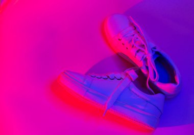 Soyut parlak arka planda modaya uygun beyaz spor ayakkabılar. Sıradan ayakkabılarda neon ışıkları. Violet ve kırmızı gradyan ışığı. Minimalizm, 90 'ların konsepti..