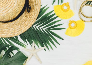 Tropik palmiye yaprakları, hasır şapka, denizyıldızı, beyaz ahşap arka planda deniz kabukları. Modayı takip eden sarı kıyafetler ve aksesuarlar. Düz yat, kapat. Yaz, tatil, tatil konsepti.