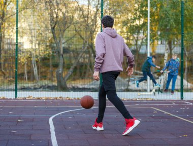 Kapüşonlu sevimli bir genç basketbol oynuyor. Top öğrenme yeteneği olan genç bir çocuk şehir sahasında top sürüyor ve ateş ediyor. Çocuklar için hobi, aktif yaşam tarzı