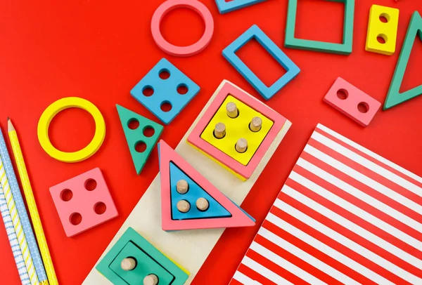 Kırmızı arka planda çok renkli ahşap bloklar. Moda bulmaca oyuncakları. Geometrik şekiller: kare, daire, üçgen, dikdörtgen. Anaokulu, anaokulu ya da kreş için eğitici oyuncaklar. Okula geri dön.