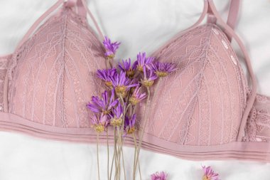 Yatakta seksi kadın iç çamaşırları ve çiçekler. Pembe sutyen, beyaz çarşaflı dantel iç çamaşırı. Güzellik blogu konsepti. Üst manzara, düz uzanma