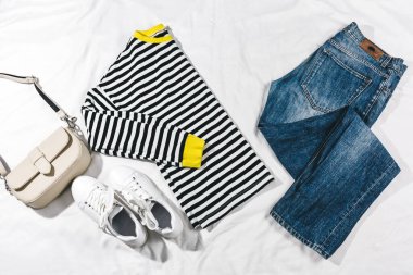 Mavi kot ve ceket, beyaz yatakta çanta ve beyaz spor ayakkabılar. Kadın tarzı yaz ya da bahar kıyafeti. Moda kıyafetleri. Düz yatış, üst görünüm.