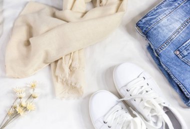Mavi kot eşarp, çanta ve beyaz yatakta beyaz spor ayakkabılar. Kadın tarzı yaz ya da bahar kıyafeti. Moda kıyafetleri. Düz yatış, üst görünüm.