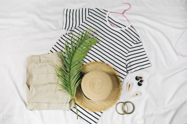 Hasır şapka, tişört, şort, beyaz arka planda sandaletler. Moda bir yaz kıyafeti. Tatiller ve tatiller için kıyafetlerle yatıyordu.