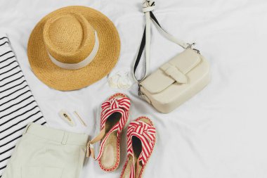 Yazlık plaj aksesuarları hasır şapka, çanta, beyaz arka planda sandaletler. Yaz konsepti, tatil kıyafetleri, yaz tatilleri.