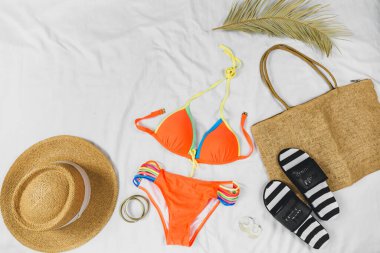 Turuncu mayo, hasır şapka, hasır çanta, beyaz arka planda parmak arası terlikler. Yaz konsepti, tatil kıyafetleri, yaz tatilleri.