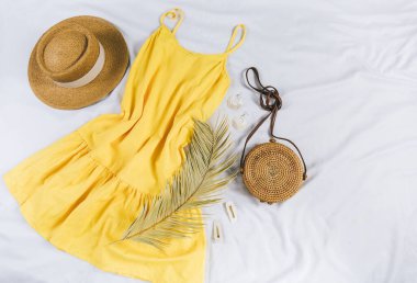 Hasır şapka, sarı elbise, beyaz arka planda saman torbası. Moda bir yaz kıyafeti. Tatiller ve tatiller için kıyafetlerle yatıyordu.