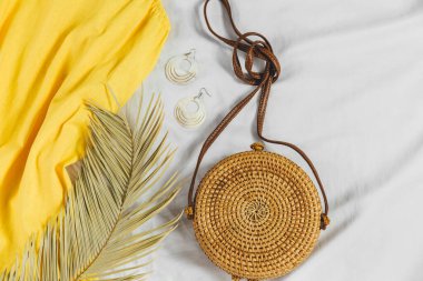 Hasır şapka, sarı elbise, beyaz arka planda saman torbası. Moda bir yaz kıyafeti. Tatiller ve tatiller için kıyafetlerle yatıyordu.