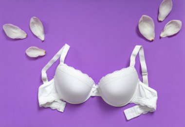 Menekşe arka planda beyaz sütyen. Sütyen, mor bir arka planda dantel iç çamaşırı. Güzellik blogu konsepti. Üst manzara, düz uzanma 