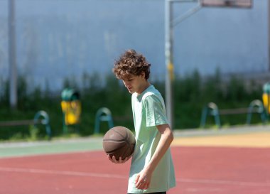 Basketbol oynayan genç, gülümseyen, neşeli. Basketbol topu olan zinde bir çocuk. Sahada top süren çocuk.