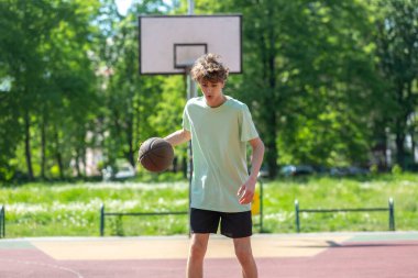 Basketbol oynayan genç, gülümseyen, neşeli. Basketbol topu olan zinde bir çocuk. Sahada top süren çocuk.