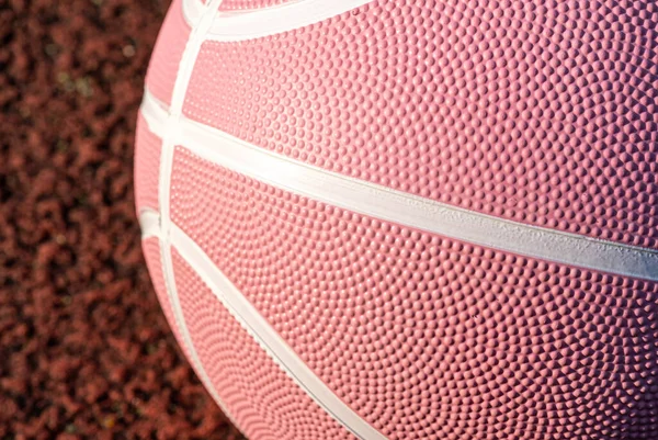 Pink basketball ball on the ground. Close-up ball on the red court. Basketball on the street or indoor court. Sports gear without people. Minimalism. Template, sport background