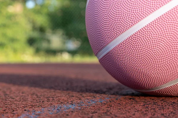 Pink basketball ball on the ground. Close-up ball on the red court. Basketball on the street or indoor court. Sports gear without people. Minimalism. Template, sport background