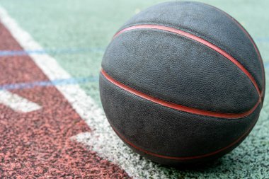 Black basketball ball on the ground. Close-up ball on the red court. Basketball on the street or indoor court. Sports gear without people. Minimalism. Template, sport background