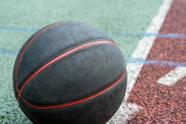 Black basketball ball on the ground. Close-up ball on the red court. Basketball on the street or indoor court. Sports gear without people. Minimalism. Template, sport background