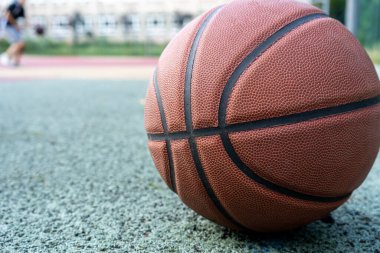 Orange basketball ball on the ground. Close-up ball on the red court. Basketball on the street or indoor court. Sports gear without people. Minimalism. Template, sport background