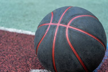 Black basketball ball on the ground. Close-up ball on the red court. Basketball on the street or indoor court. Sports gear without people. Minimalism. Template, sport background
