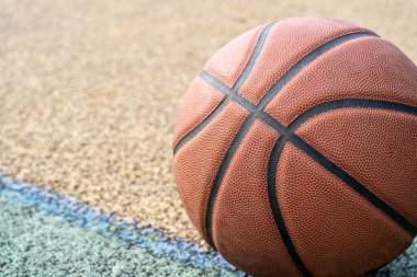 Orange basketball ball on the ground. Close-up ball on the red court. Basketball on the street or indoor court. Sports gear without people. Minimalism. Template, sport background
