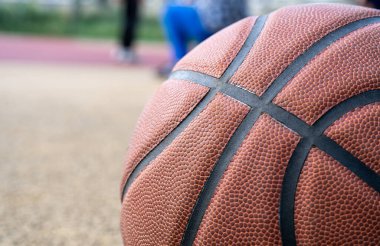 Orange basketball ball on the ground. Close-up ball on the red court. Basketball on the street or indoor court. Sports gear without people. Minimalism. Template, sport background