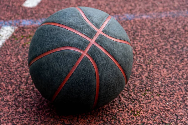 Black basketball ball on the ground. Close-up ball on the red court. Basketball on the street or indoor court. Sports gear without people. Minimalism. Template, sport background