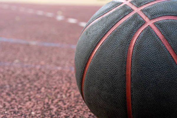 Black basketball ball on the ground. Close-up ball on the red court. Basketball on the street or indoor court. Sports gear without people. Minimalism. Template, sport background