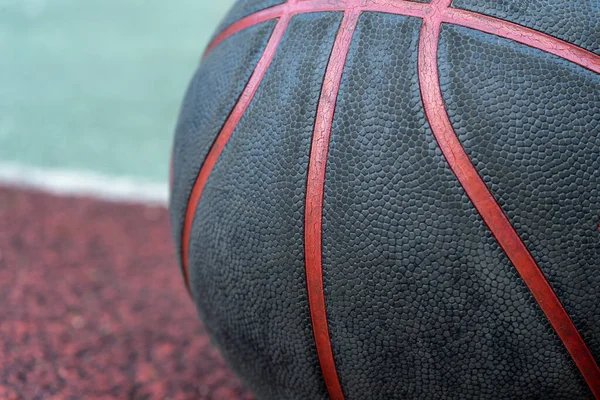 Black basketball ball on the ground. Close-up ball on the red court. Basketball on the street or indoor court. Sports gear without people. Minimalism. Template, sport background